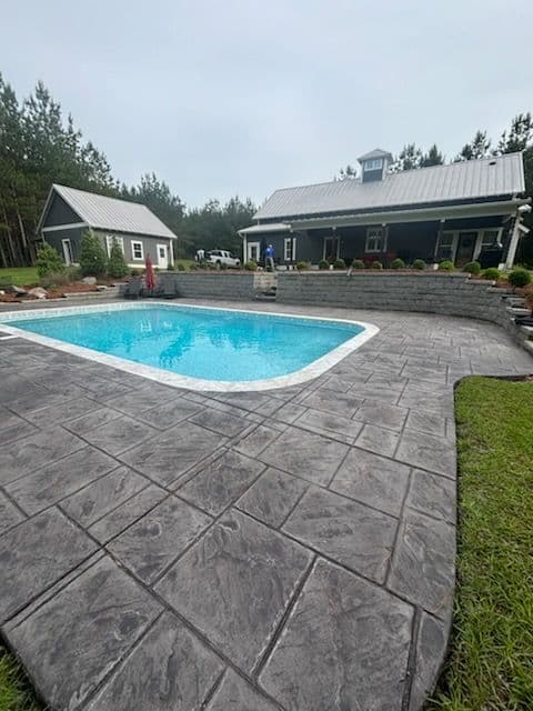 Modern backyard with a blue pool, stamped concrete patio, and rustic-style house.