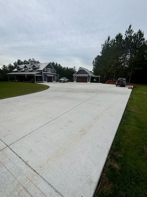 Newly poured concrete driveway leading to a modern house and garages surrounded by trees.