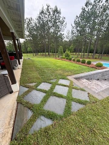 Lush backyard with stone pathway, green lawn, and swimming pool surrounded by trees.