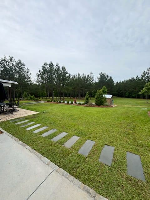 Lush green yard with stone path, trees in background, and a cozy seating area.