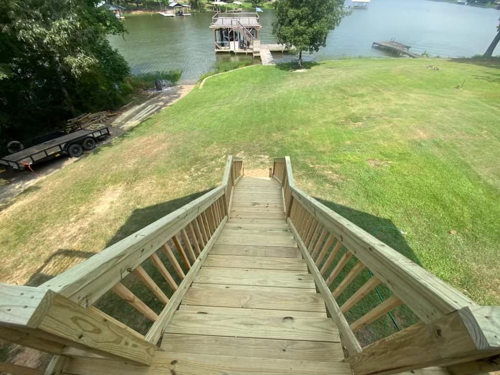 Wooden steps leading down to a serene lake with boats and green grass in the background.