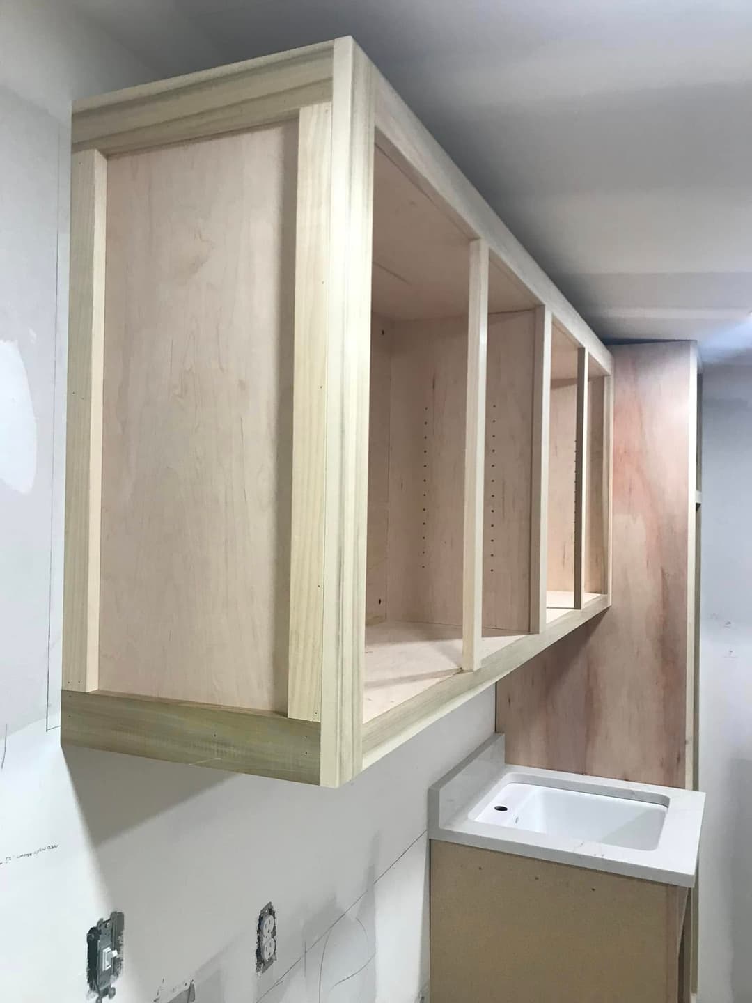 Unfinished wooden kitchen cabinet with a sink below, against a light wall.