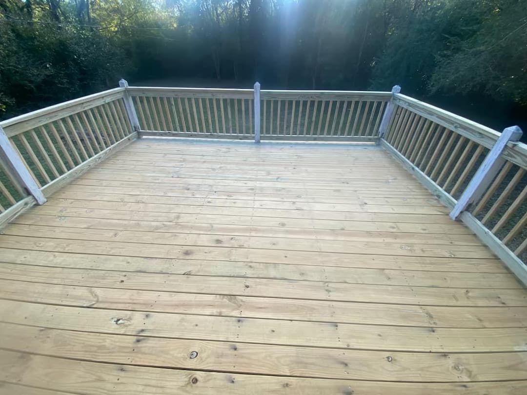 Spacious wooden deck overlooking a green wooded area, perfect for outdoor relaxation.
