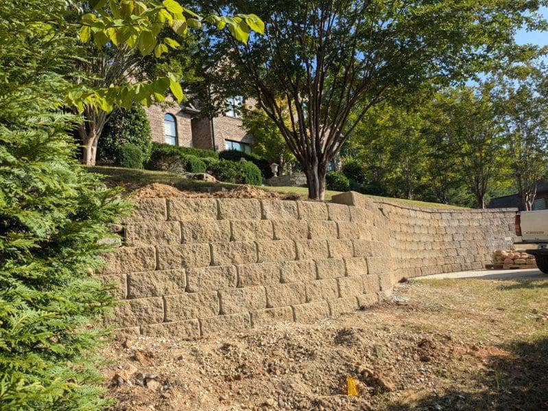 Retaining wall construction in a landscaped yard with trees and a home in the background.