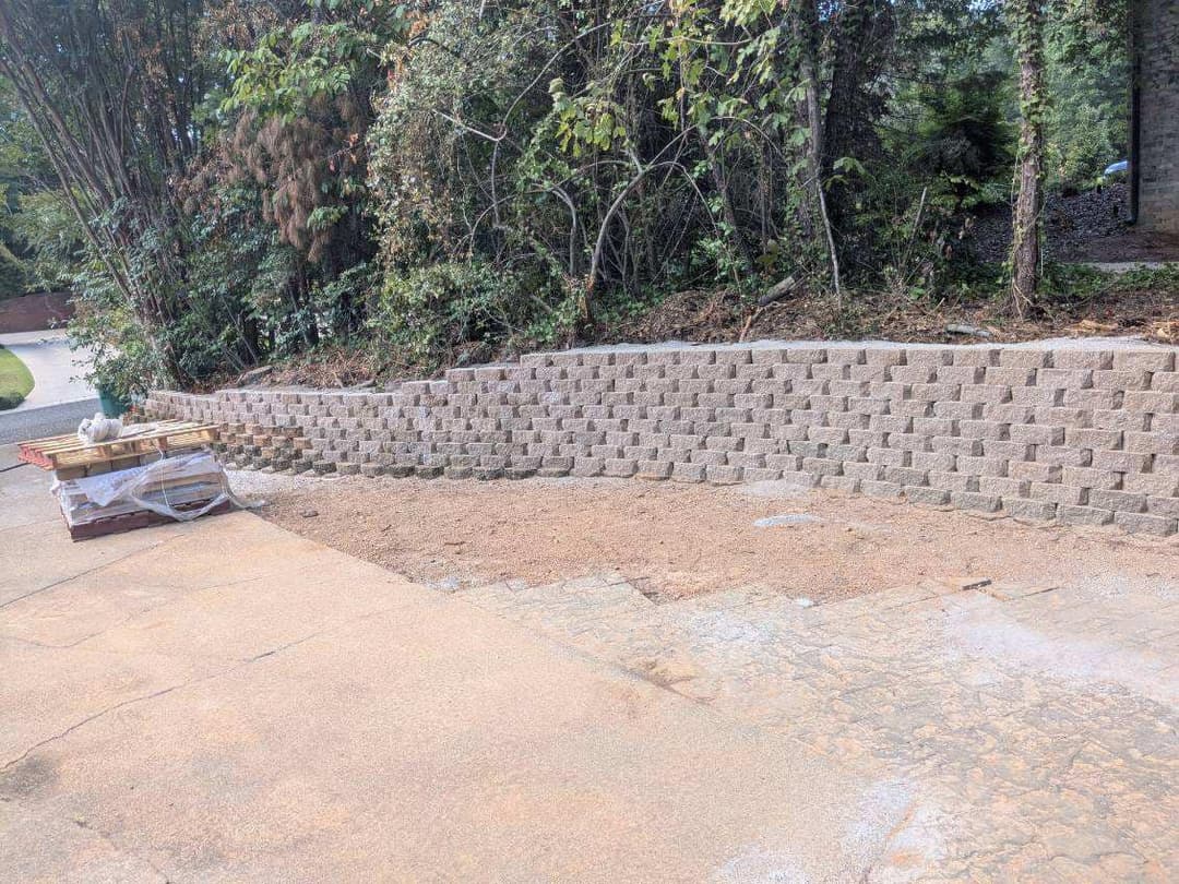 Retaining wall made of interlocking stones with a gravel base in a landscaped area.