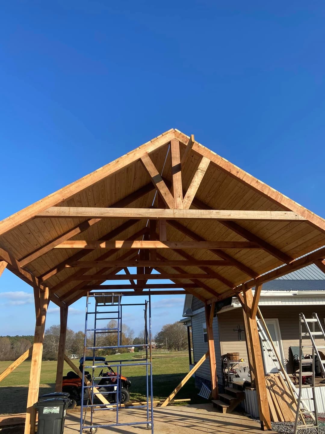 Timber-frame construction of a building roof under a clear blue sky.
