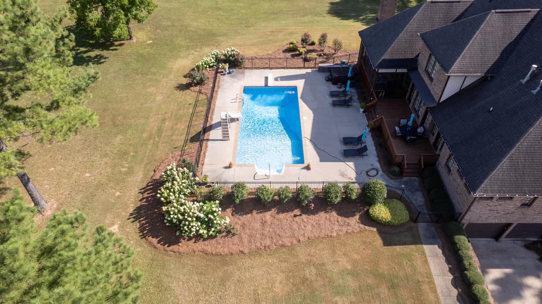 Aerial view of a landscaped backyard with a swimming pool surrounded by greenery and a house.