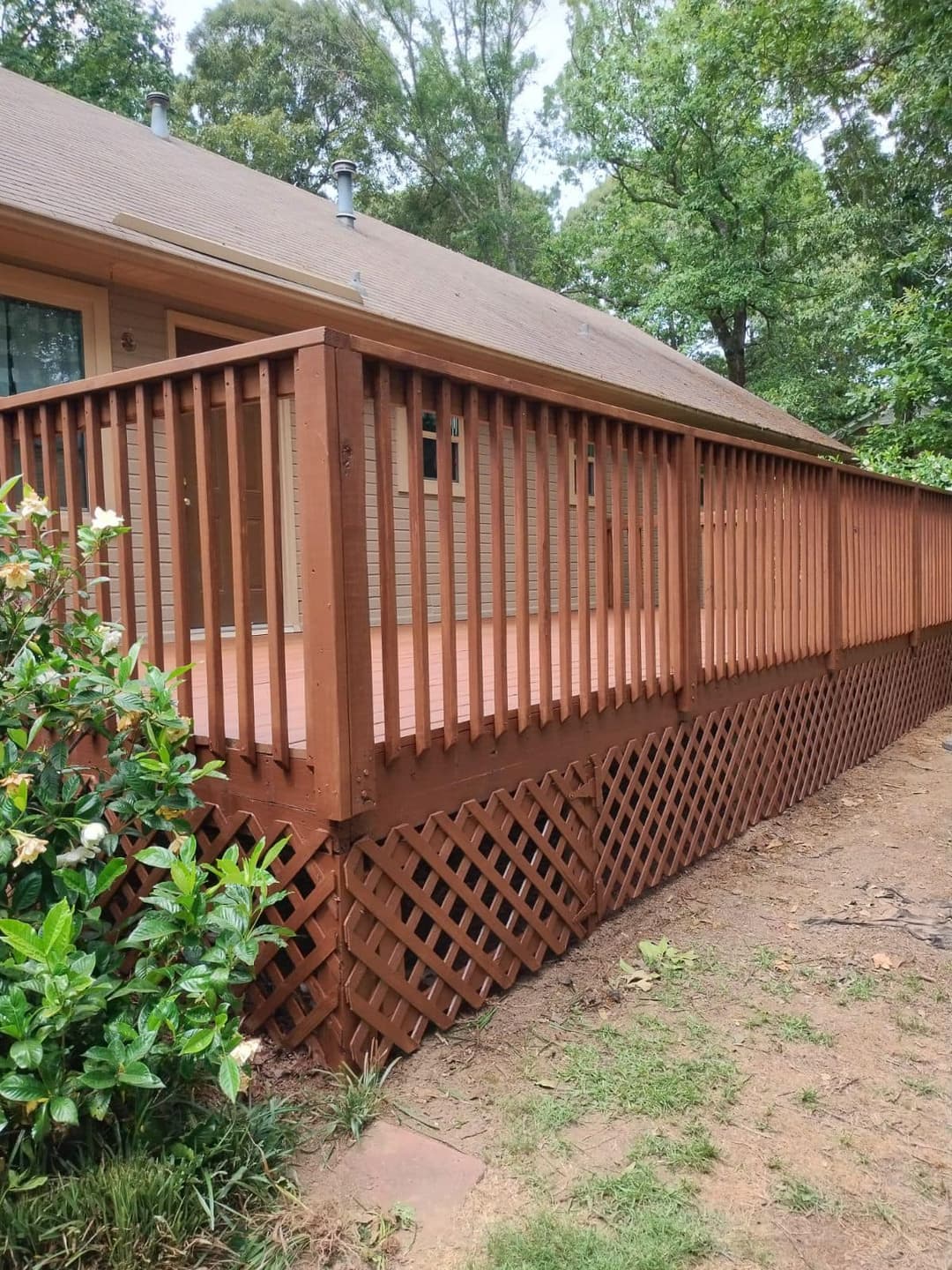 Wooden deck with railings and lattice, surrounded by greenery and trees in a residential setting.