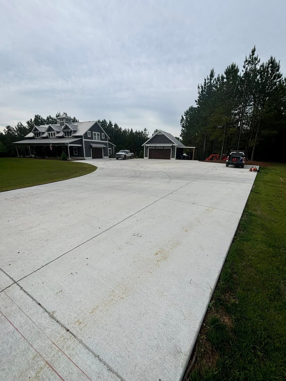 Newly poured concrete driveway leading to a stylish home surrounded by greenery.