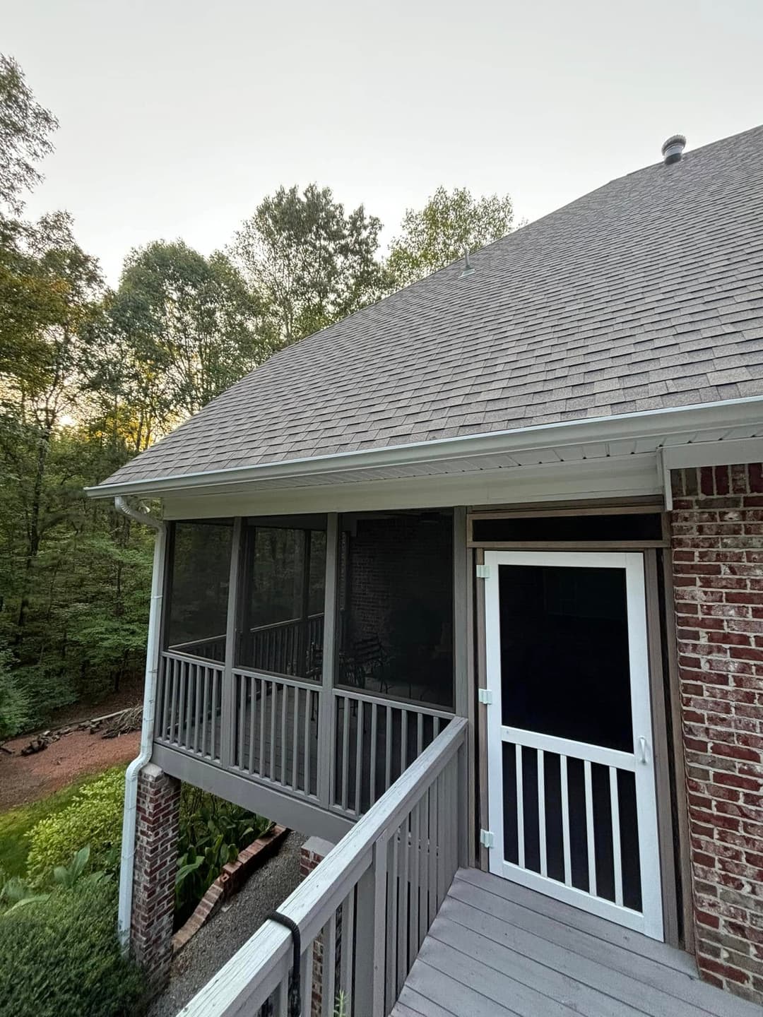 Screened porch view of a house surrounded by trees during sunset.