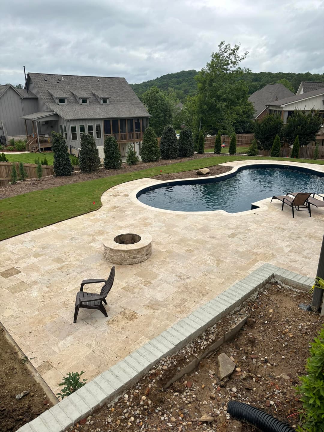 Backyard oasis with in-ground pool, fire pit, and landscaped lawn under cloudy skies.