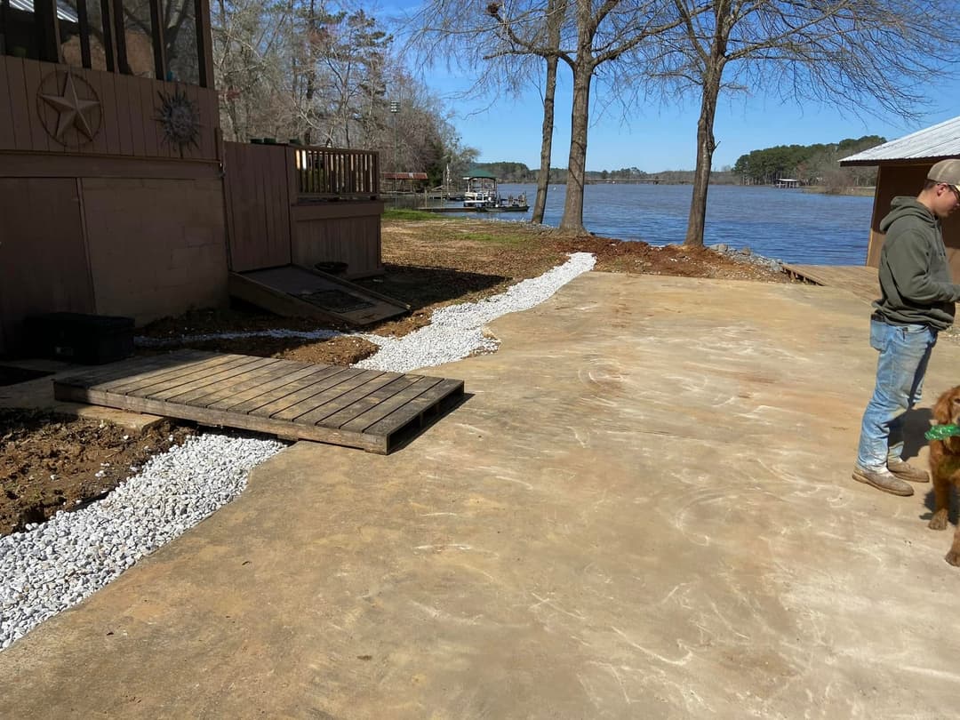 Lakeside property with gravel pathway, wooden ramp, and a person with a dog by the water.