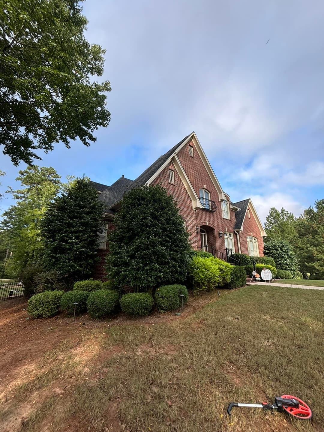 Elegant brick house with manicured shrubs and trees on a sunny day.