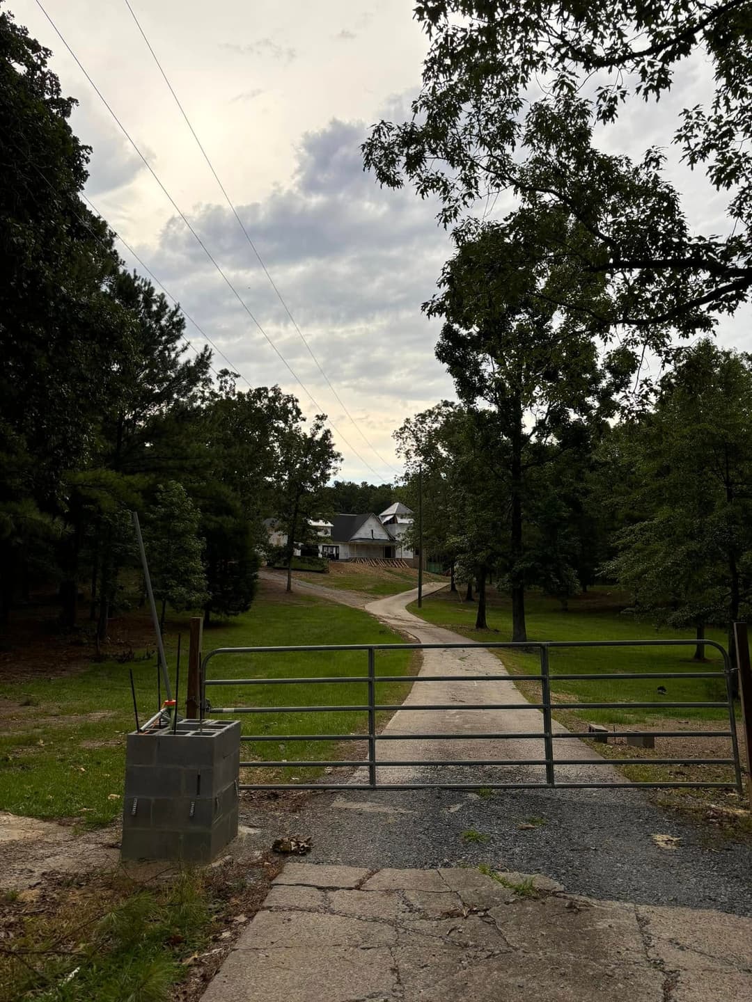 Gravel driveway leading to a house, framed by trees and a gated entrance on a cloudy day.