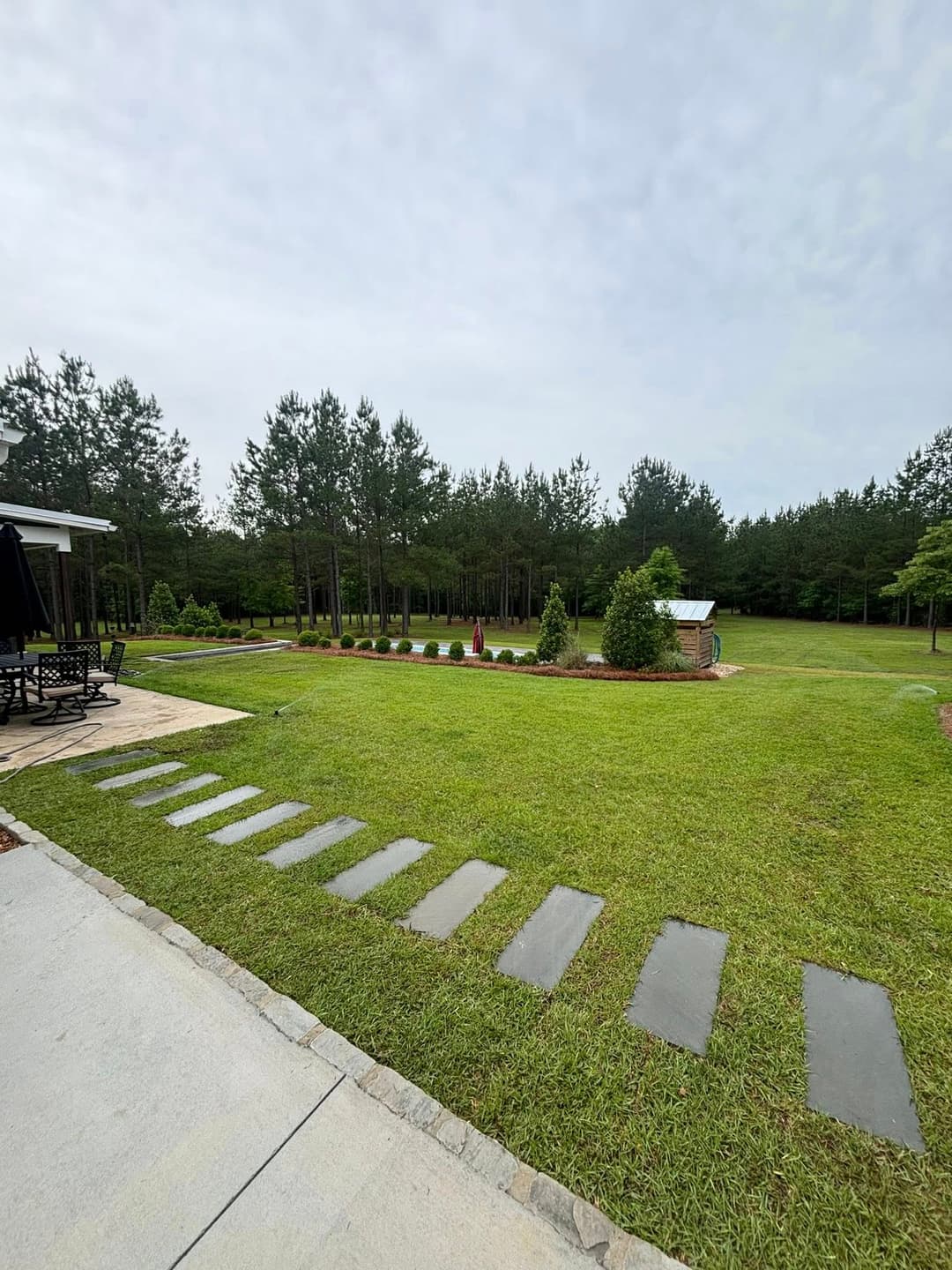 Lush green yard with stone pathway, surrounded by trees and landscaped garden area.