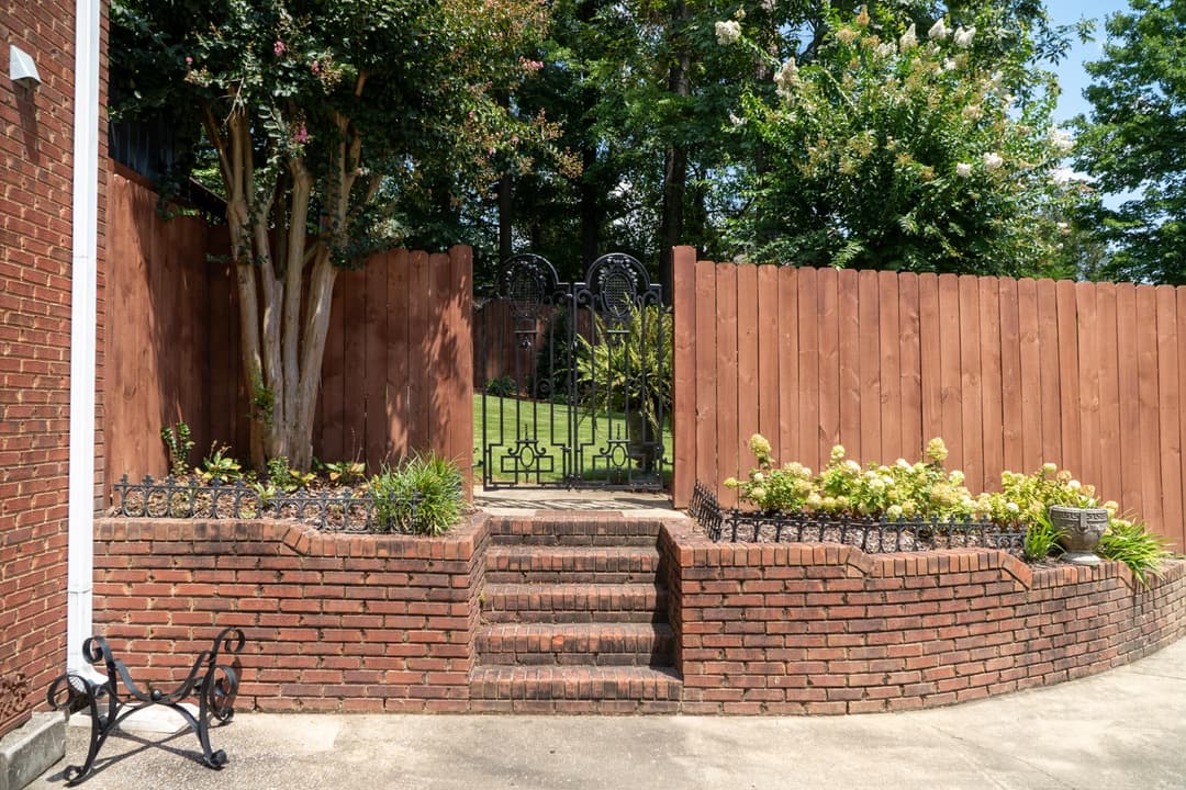 Elegant brick staircase leading to ornate black gates in a landscaped garden setting.