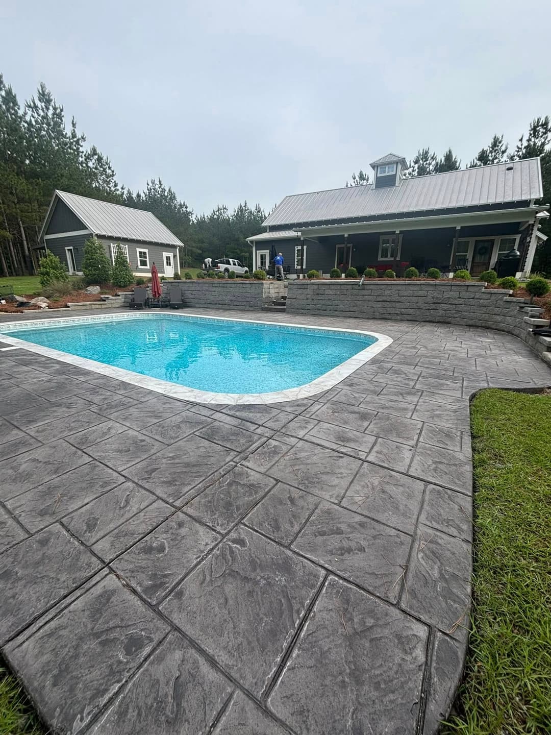 Inviting backyard pool with stamped concrete patio and surrounded by greenery and a house.
