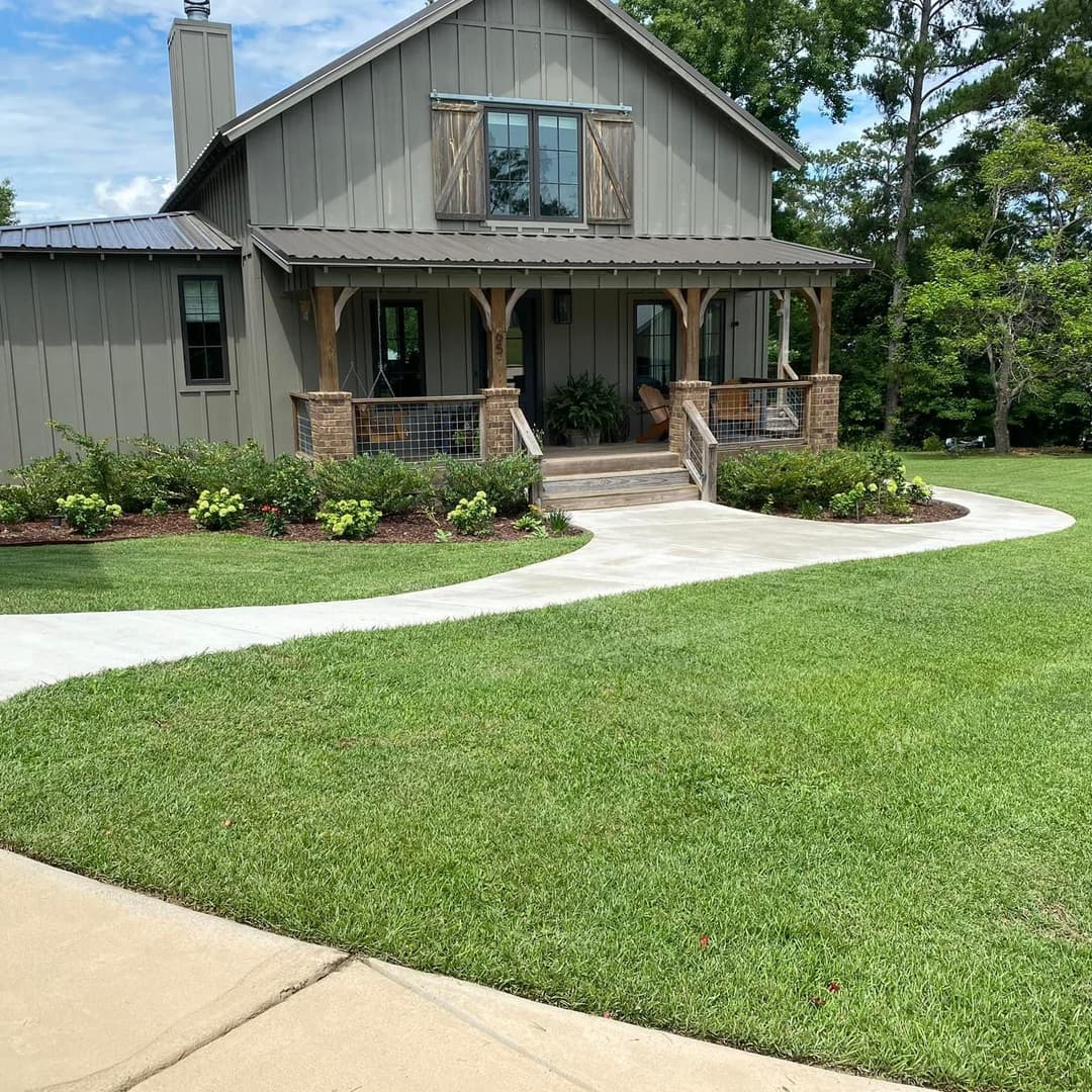 Modern gray house with a porch, landscaped yard, and curved pathway on a sunny day.