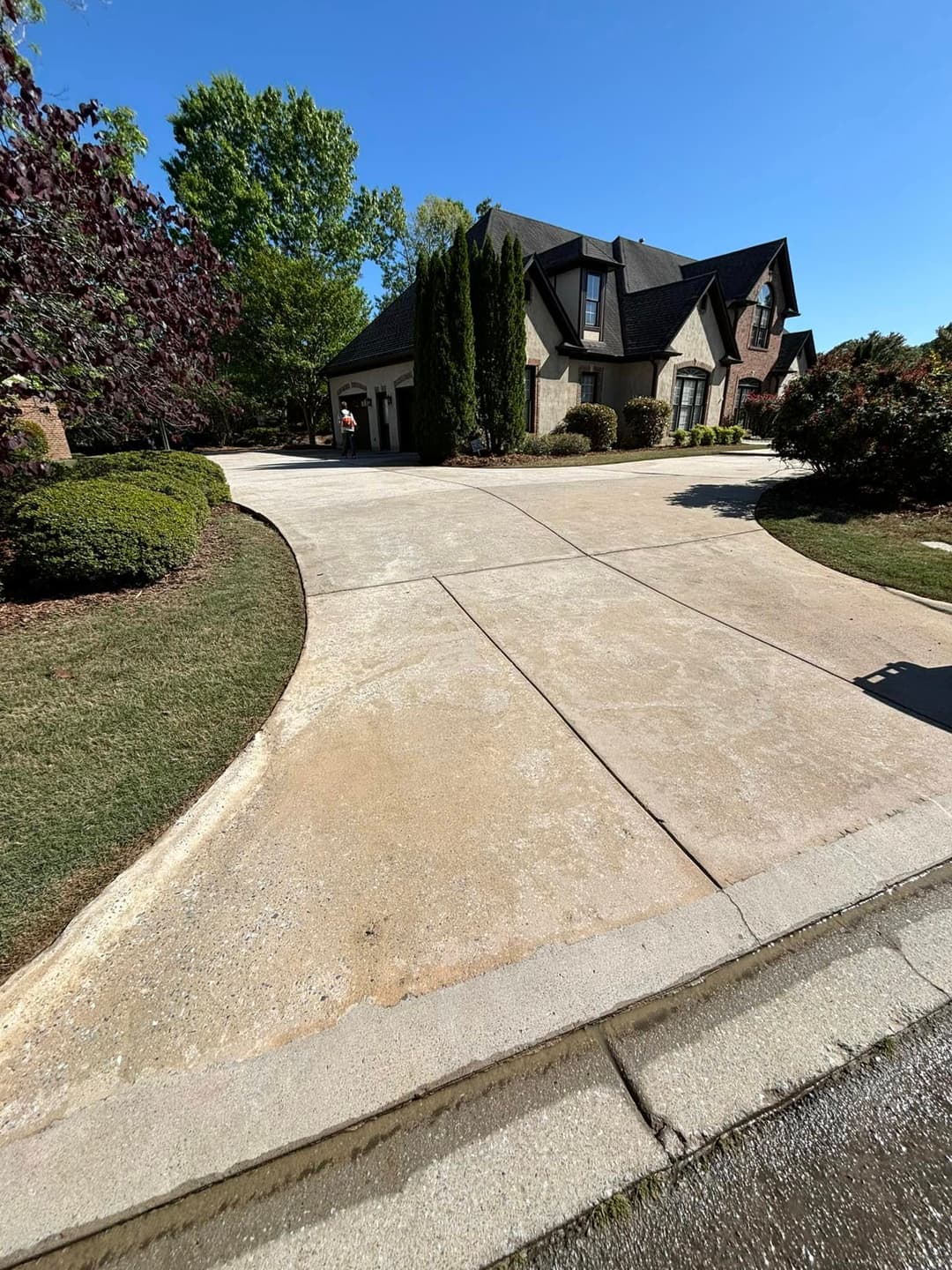 Residential driveway leading to a house with landscaped greenery under a clear blue sky.