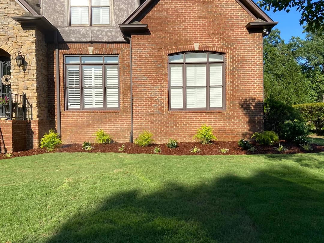 Well-maintained brick house with landscaped garden and green lawn under bright sunlight.