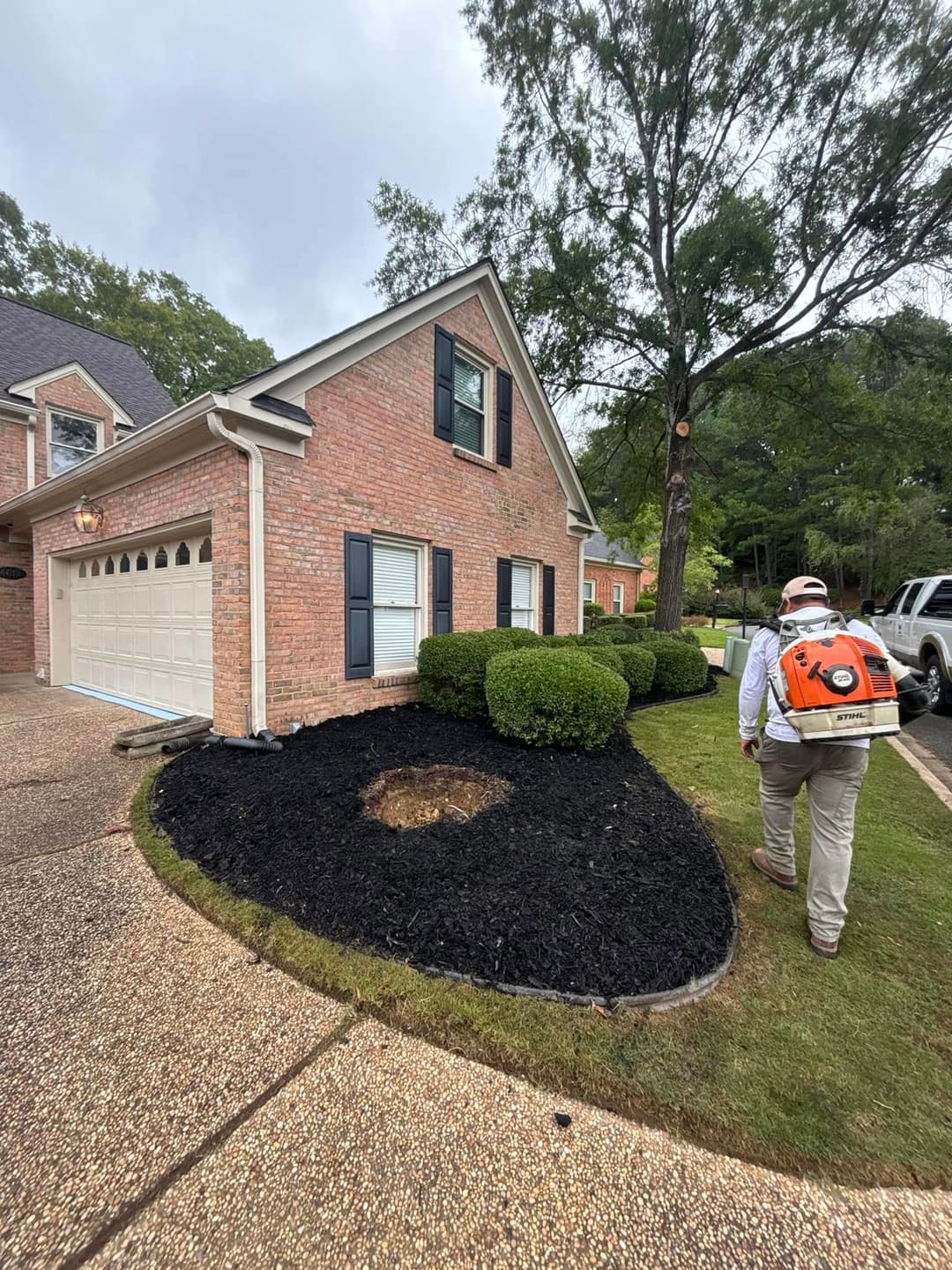 Landscaper with backpack blower working on yard maintenance near a brick house.