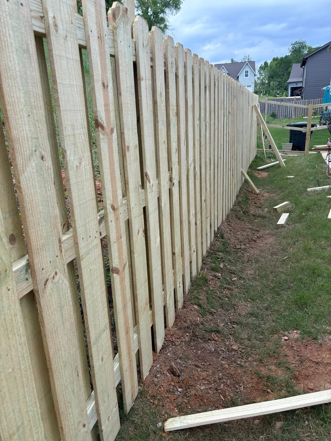 Wooden fence construction in a residential yard, with uninstalled boards on the ground.