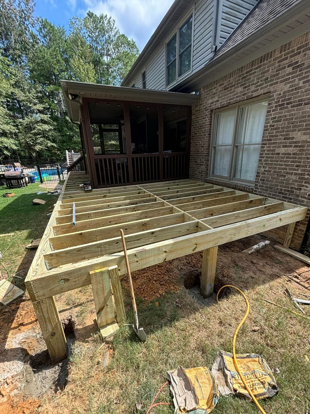New wooden deck framing under construction next to a house, surrounded by greenery.