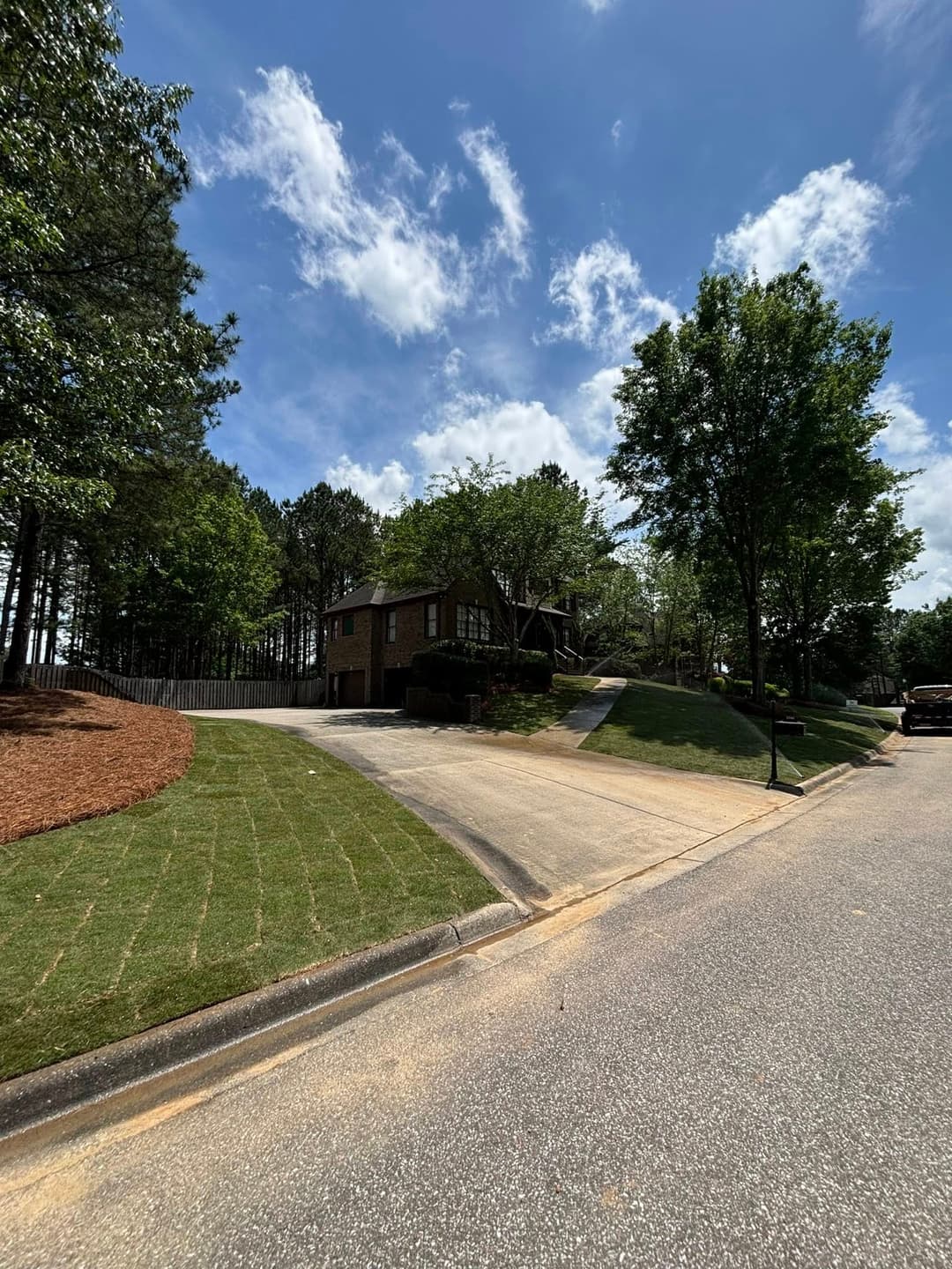 Two-story house on a sloped lot surrounded by trees and blue sky on a sunny day.