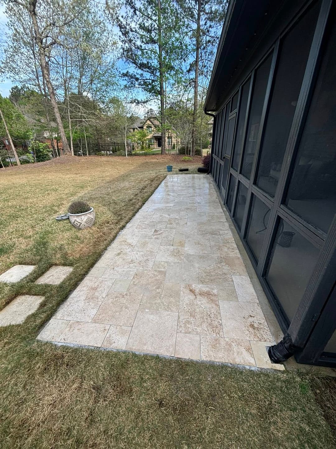 Patio area with stone tiles, grass, and landscaping beside a house.