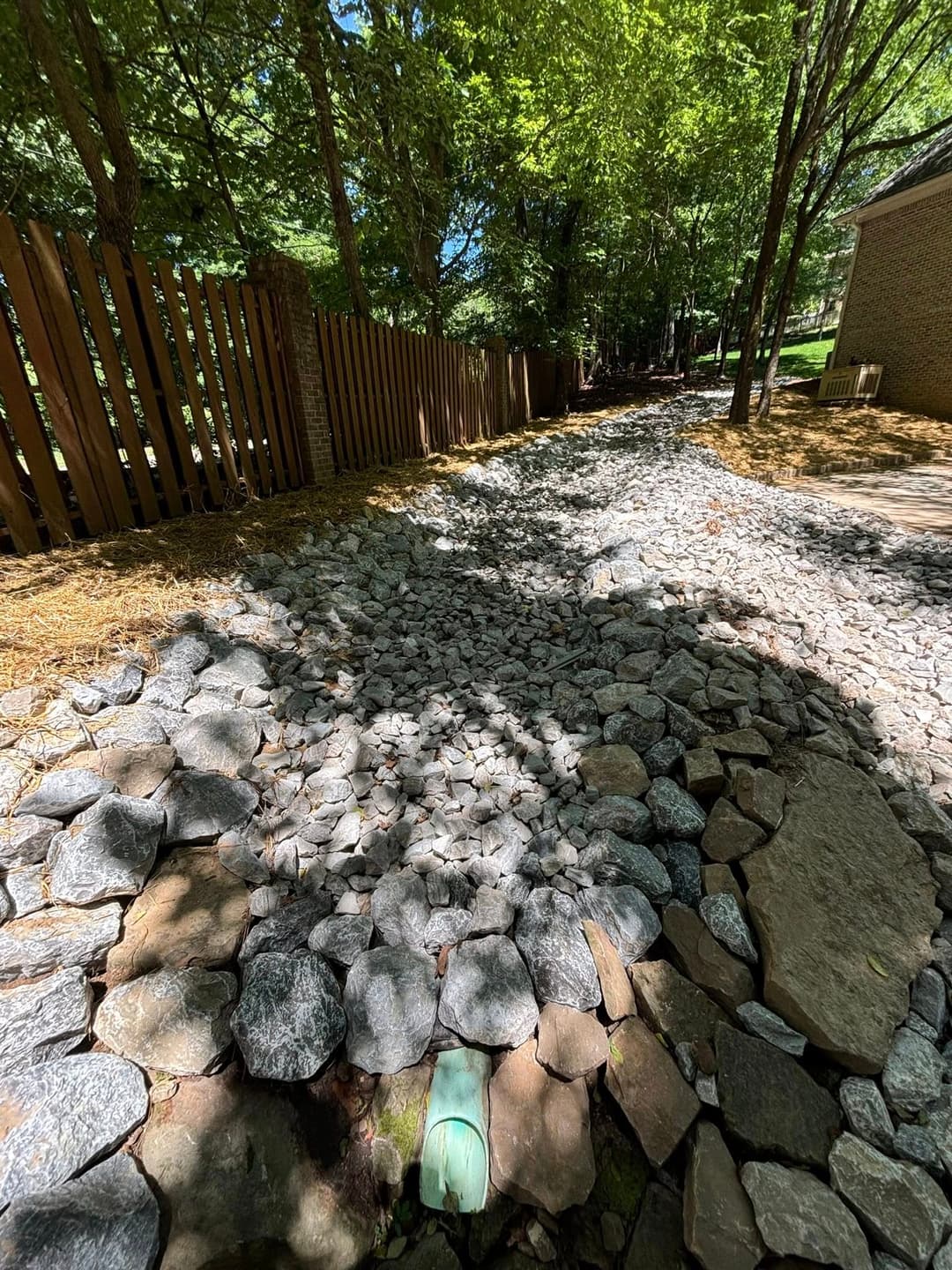 Gravel pathway bordered by trees and a wooden fence in a serene outdoor setting.