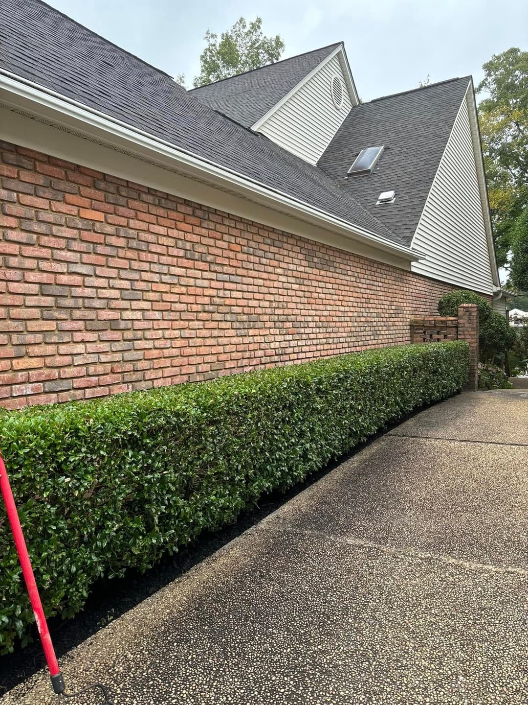 Brick house exterior with well-trimmed hedges and a paved driveway.