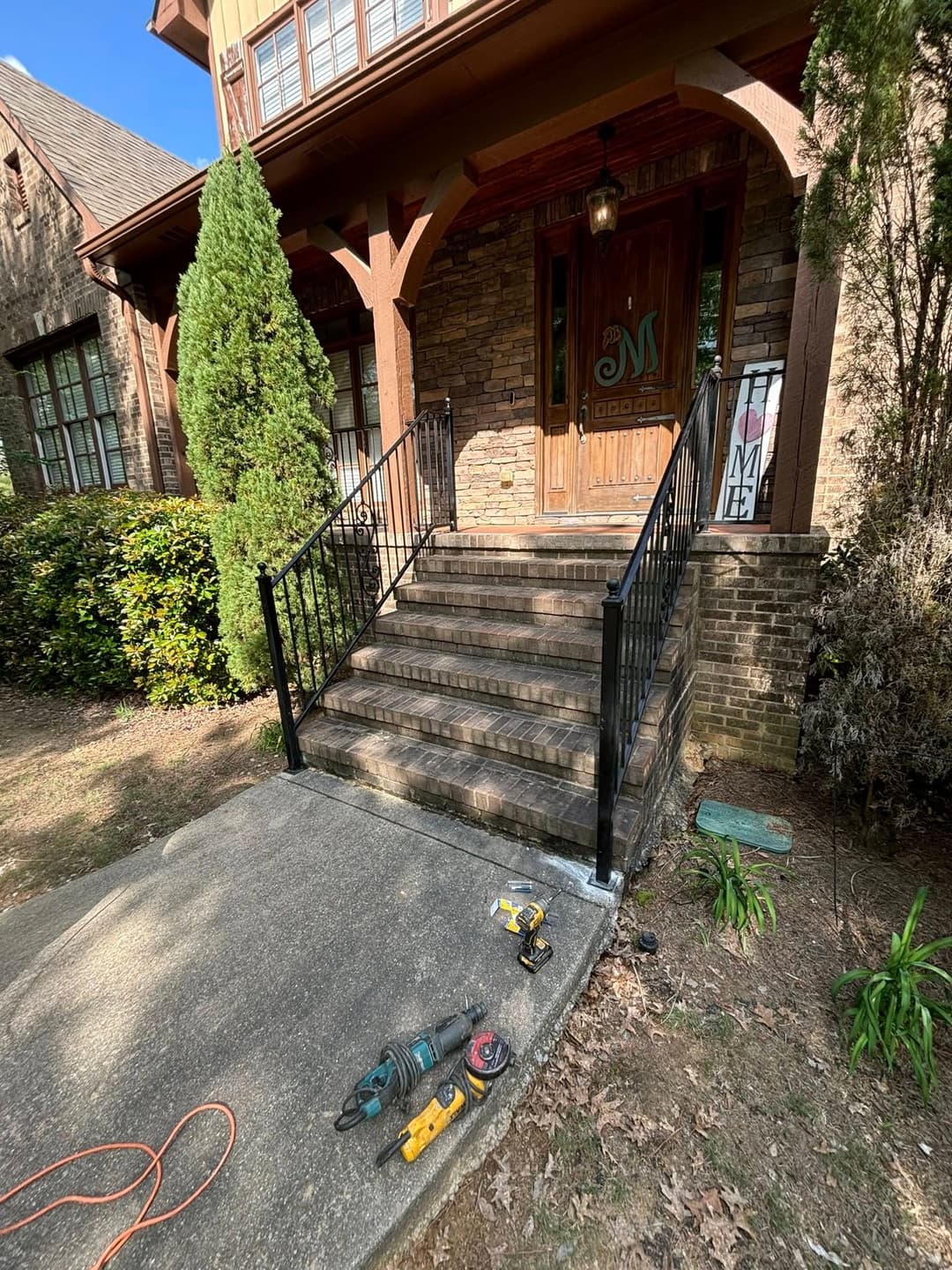 Front entrance with stone steps and metal railing, featuring tools on the concrete walkway.