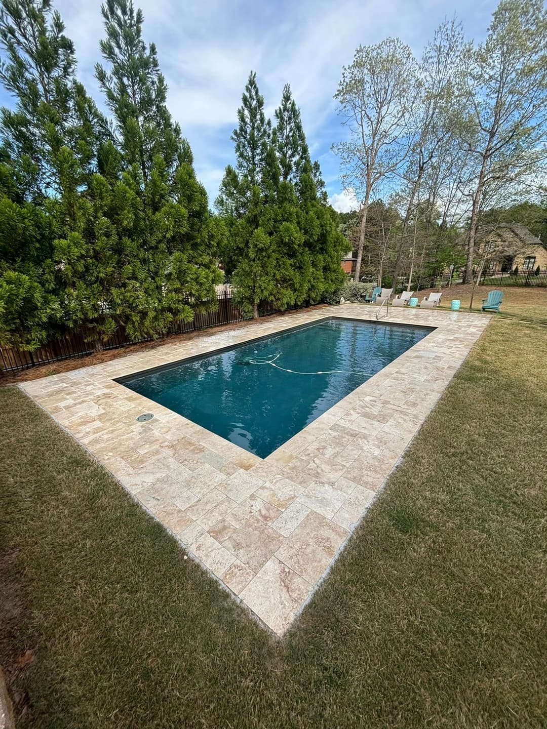 Spacious outdoor swimming pool surrounded by lush greenery and patio chairs.
