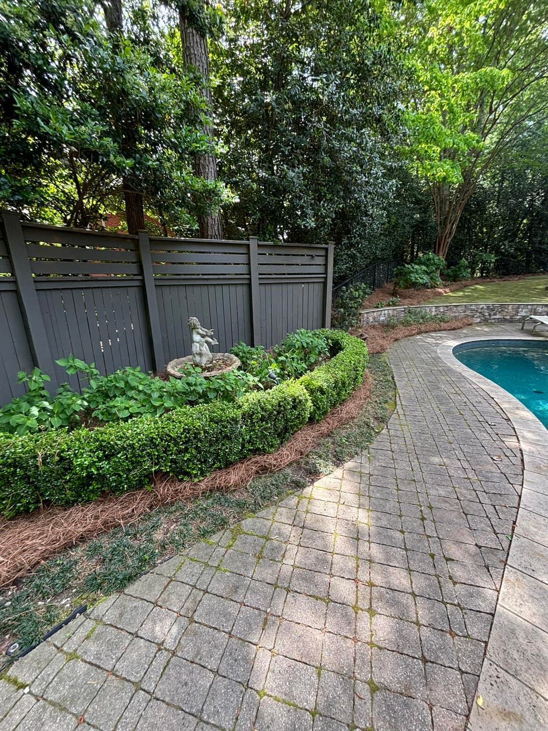 Garden path with greenery and a statue near a swimming pool in a serene backyard setting.