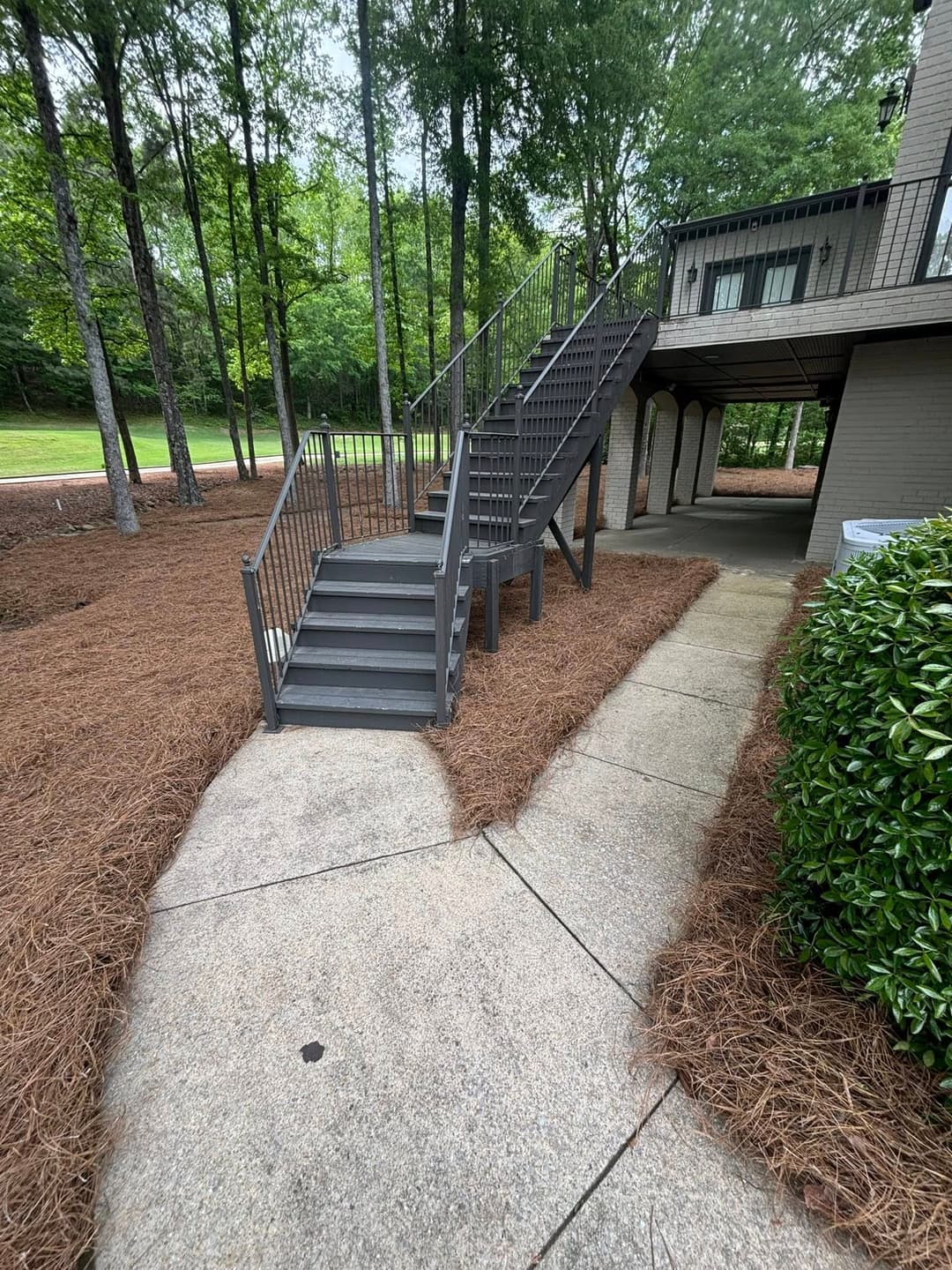 Exterior view of a building featuring a gray staircase and landscaped pathway surrounded by trees.