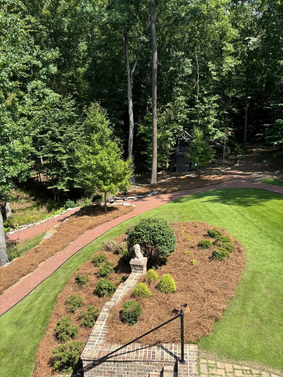Lush green garden with manicured shrubs and a stone pathway surrounded by trees.