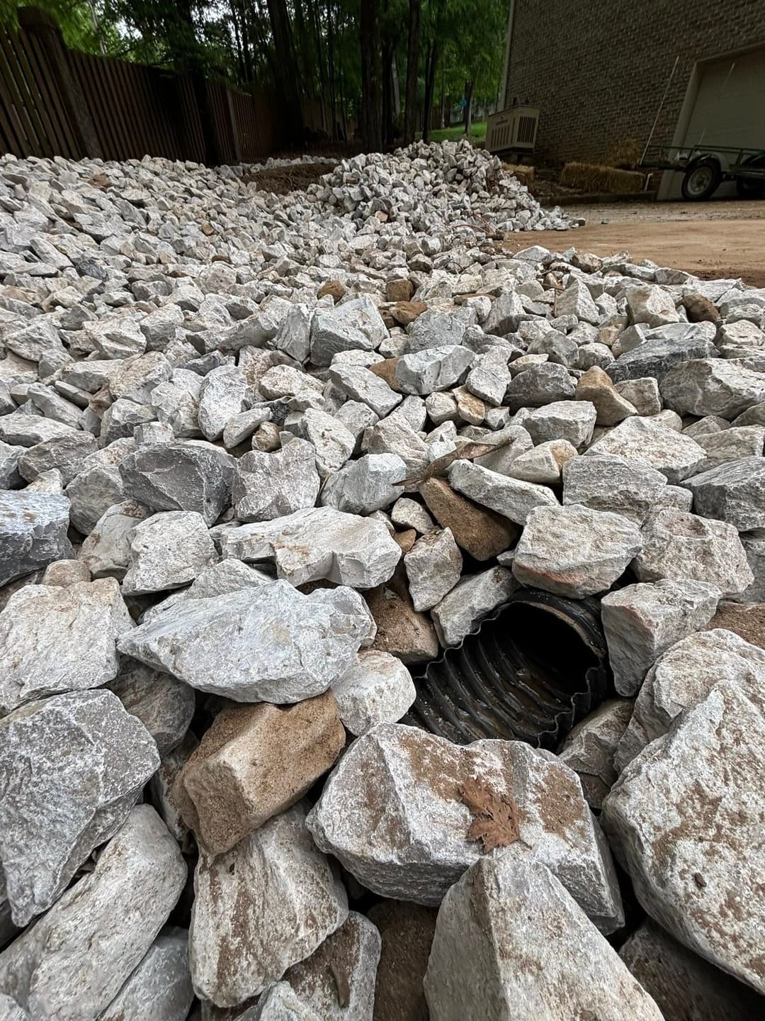 Rock landscaping with drainage pipe among gray stones in outdoor setting.