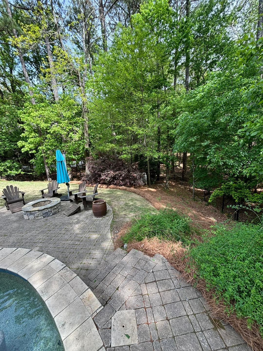 Backyard oasis with a stone fire pit, seating area, and lush green trees. Perfect for relaxing.