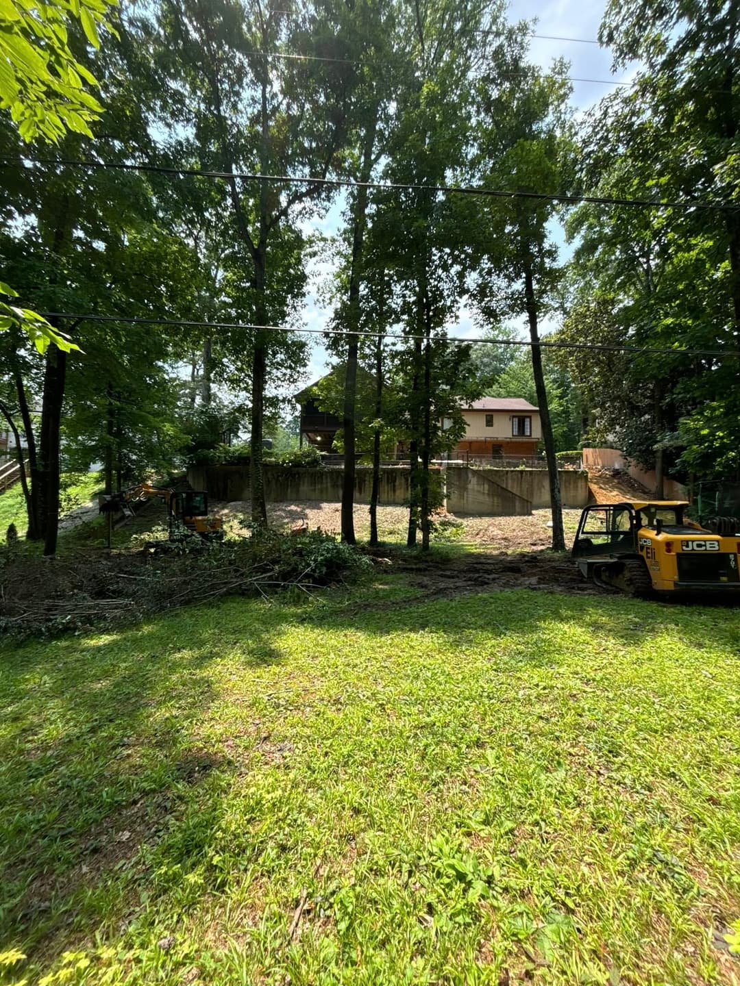 Cleared area behind a house, with trees and construction equipment in a forested setting.