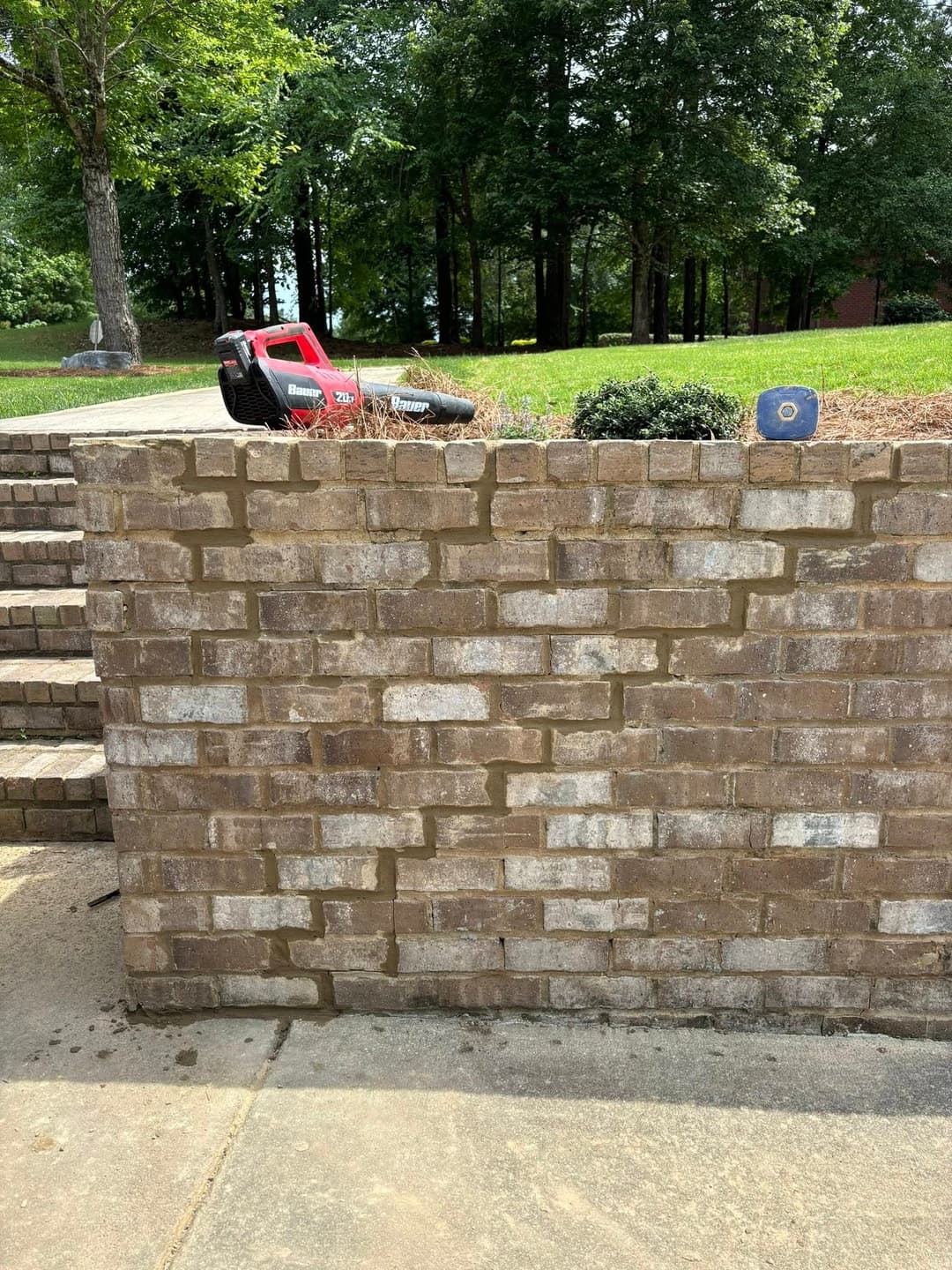 Brick wall with landscaping tools and greenery in a landscaped yard.