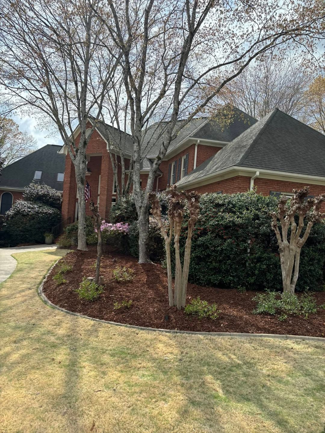 Brick house with manicured landscaping and blooming trees on a sunny day.