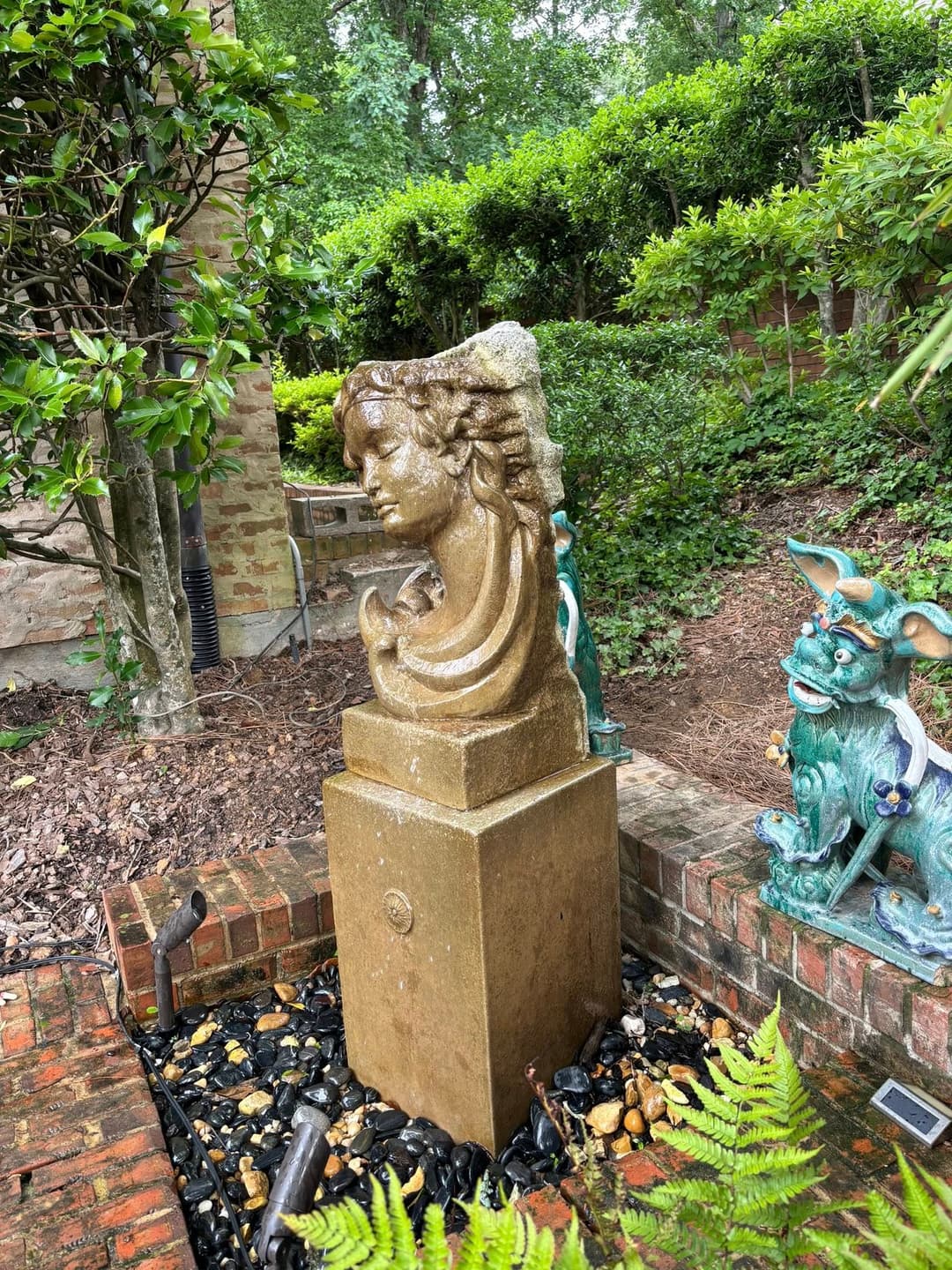 Stone sculpture of a woman surrounded by greenery in a garden setting.