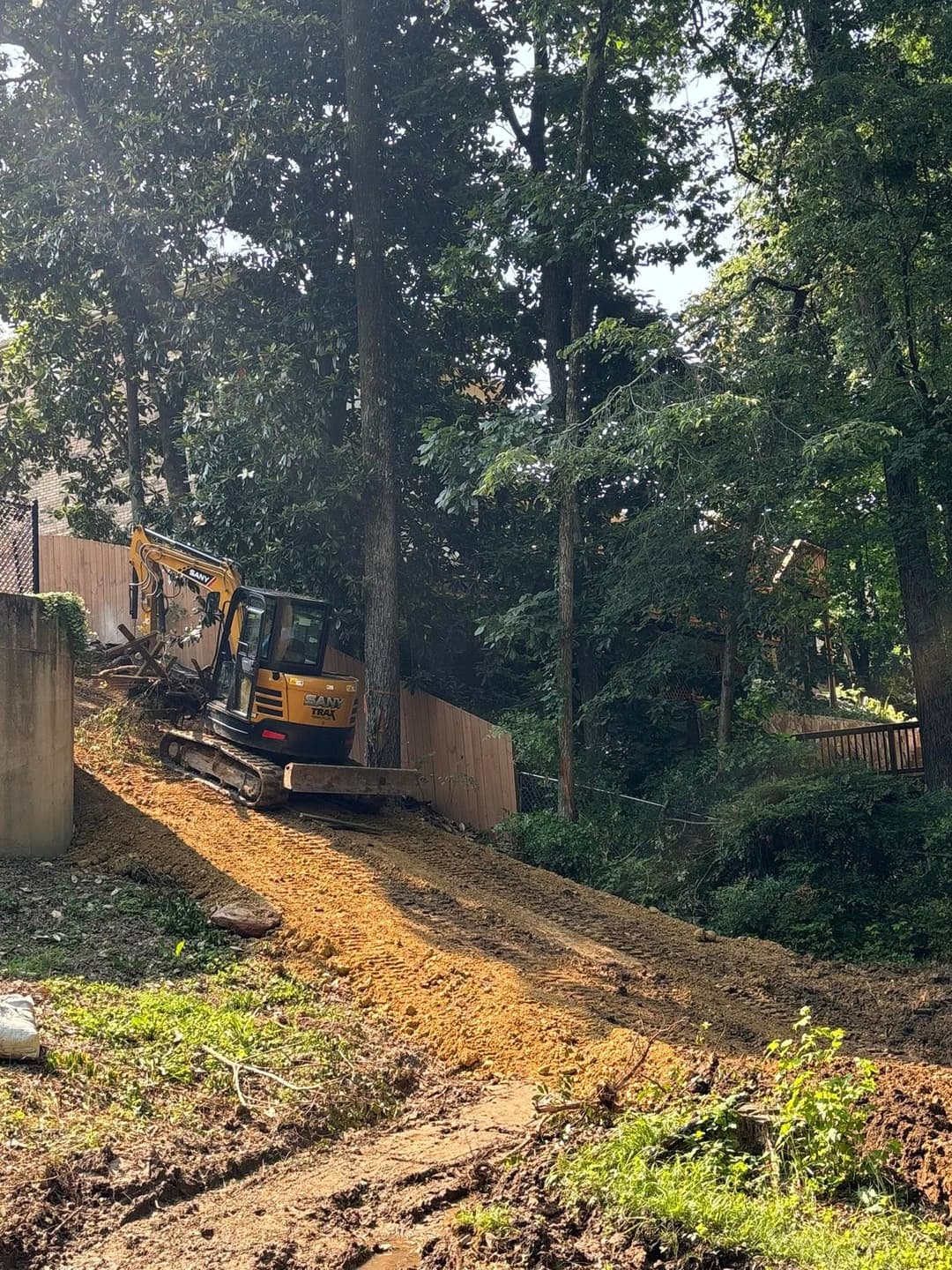 Excavator working on a sloped dirt path in wooded area for construction project.