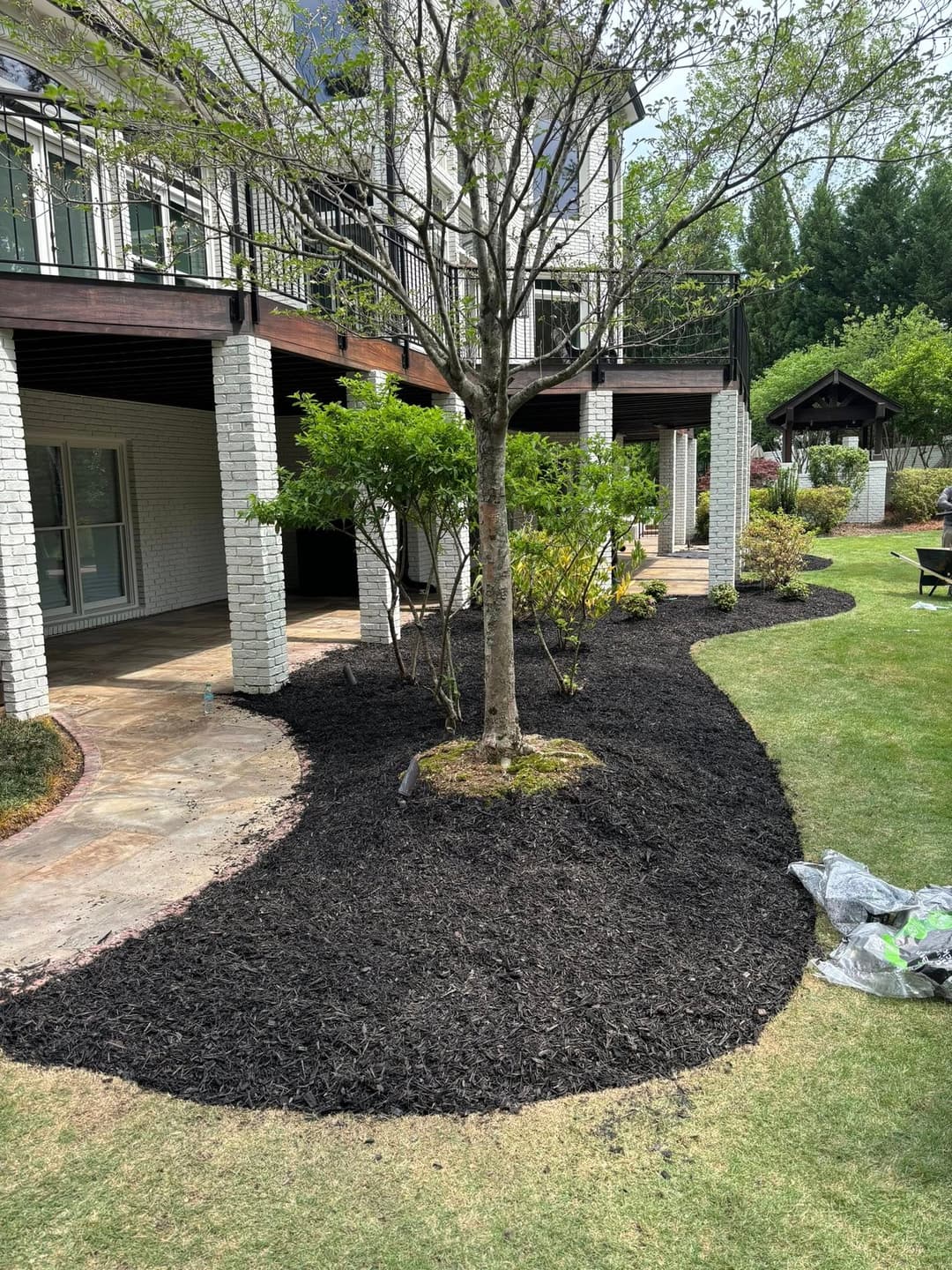 Black mulch landscaping around a tree near a patio, enhancing garden aesthetics and maintenance.