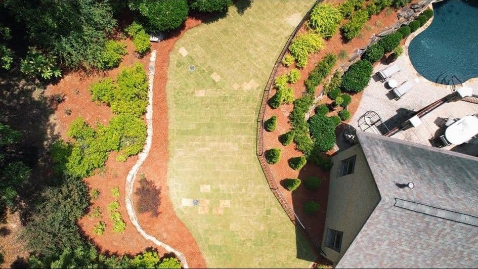 Aerial view of a landscaped backyard with a patio, pool, and neatly trimmed grass.
