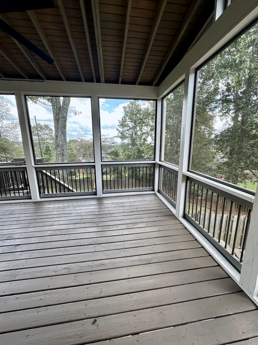 Spacious screened porch with wooden flooring and panoramic views of nature.