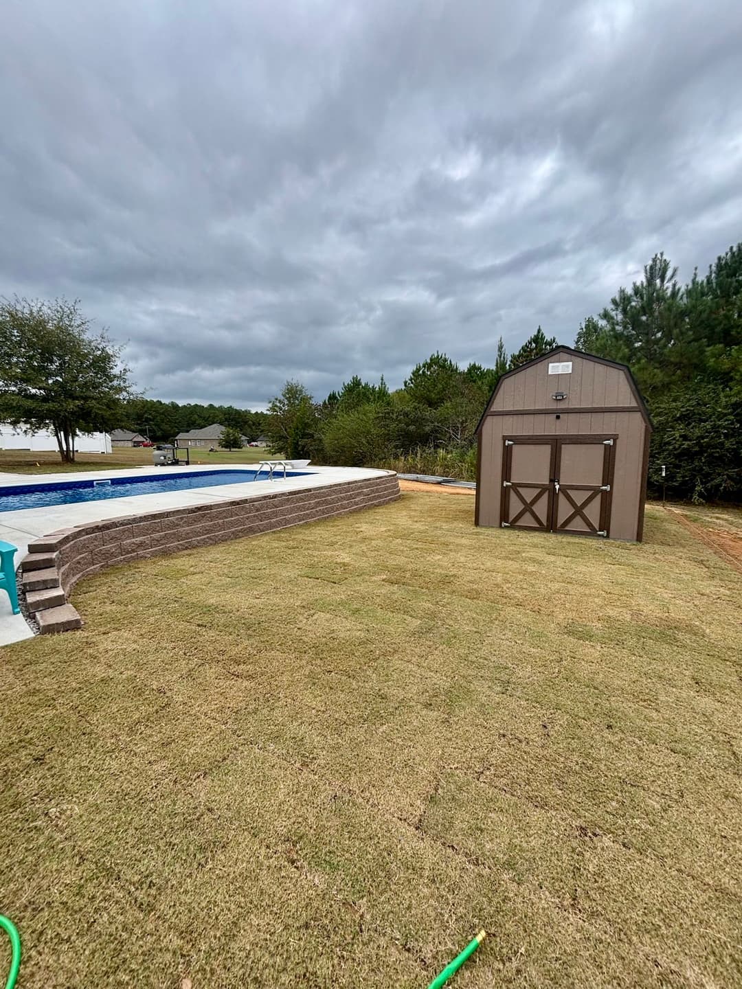 Backyard with a swimming pool, shed, and green lawn under a cloudy sky.