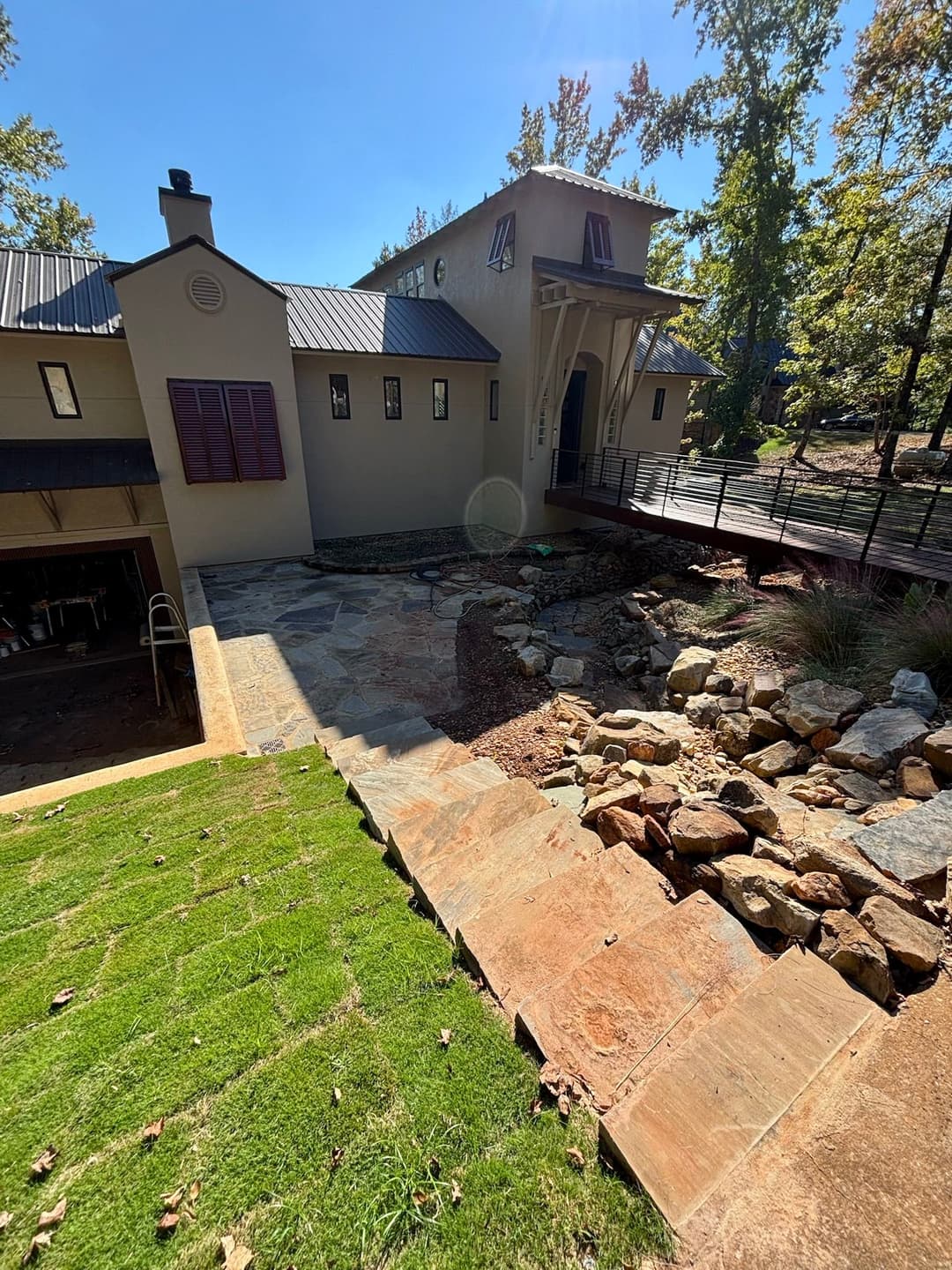 Modern house with stone pathway, landscaping, and wooden deck surrounded by trees.