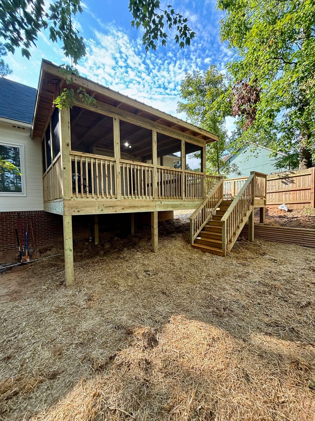 Newly built wooden deck with stairs, surrounded by greenery and clear blue sky.