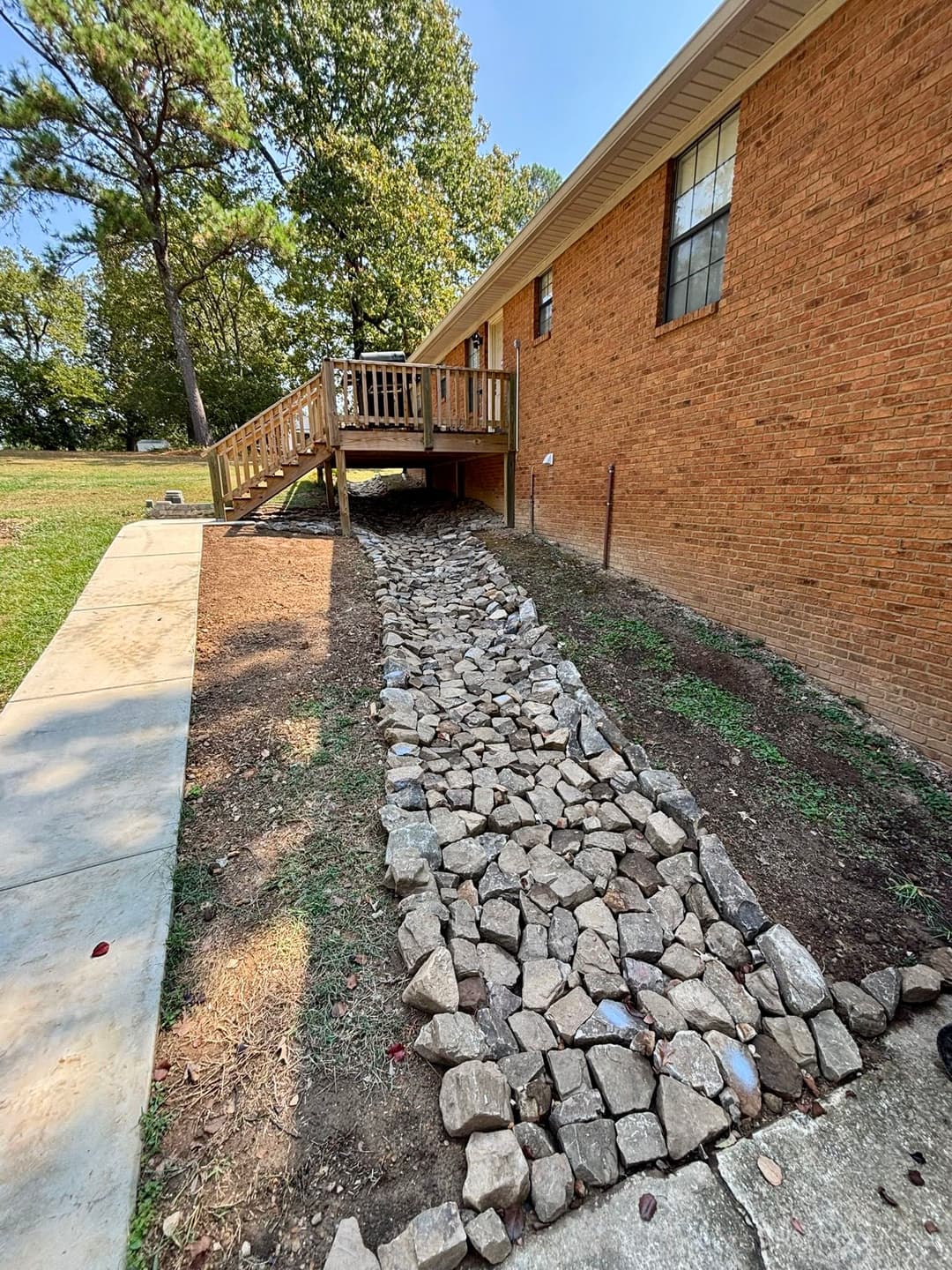 Rock pathway leading to a wooden deck at a brick house surrounded by green grass.